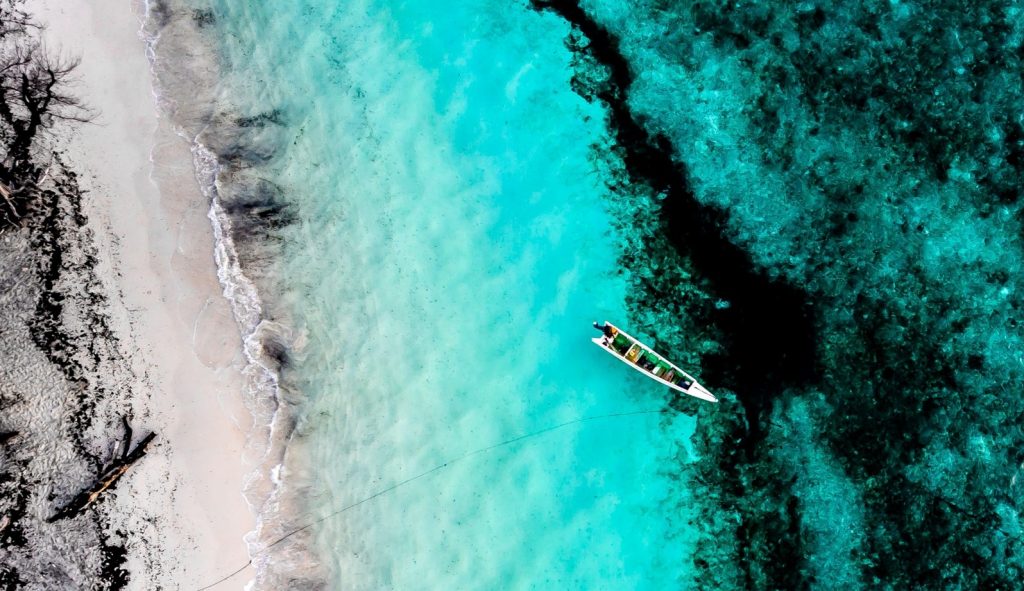 An overhead view of a boat floating near a beach shore in turquoise blue waters