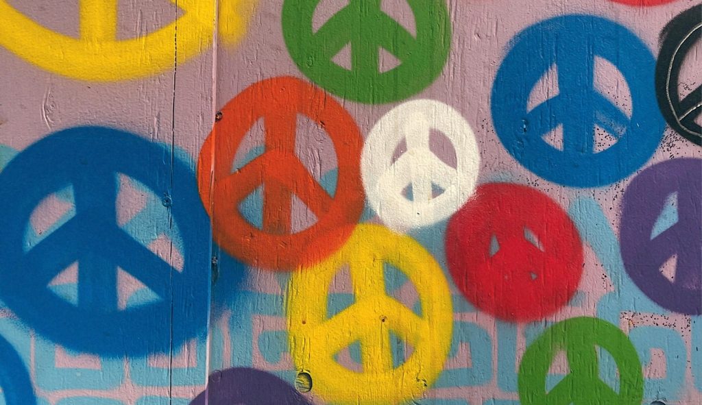 Peace symbols painted on a pink wall in various colours