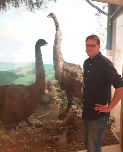 Dr Gardner stands in front of two moa models in a panorama at the Otago Museum.